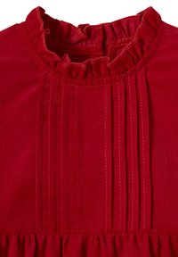 Rote Cordstoff mit vertikalen gesteppten Falten und einem Rüschendetail am Kragen.
