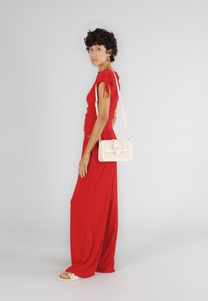 Tuta rossa con maniche corte e dettagli arricciati, abbinato a una borsa intrecciata color crema e sandali con accenti metallici.