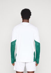 Pikkade varrukatega valge särk, millel on rohelised võrkkangast aktsendid varrukatel. Särgil on ümar kaelus ja see on valmistatud kergest, hingavast materjalist.