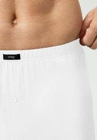 Shorts en coton blanc avec taille élastique et détail bouton. L'étiquette indique "mey." Le tissu semble lisse et légèrement réfléchissant.