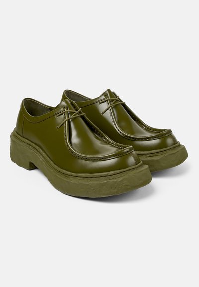 Olive green, glossy leather shoes with a rounded toe, featuring visible stitching and a thick, textured rubber sole.