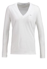 Langärmliges weißes Baumwoll-V-Ausschnitt-T-Shirt mit kleinem, gesticktem Lacoste-Logo auf der linken Brust, glatte Textur und taillierte Passform.