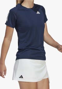 Marinblå atletisk t-shirt med kortärmar och rund halsringning, ihop med en vit kjol. Båda har Adidas-logotypen i kontrasterande färger.