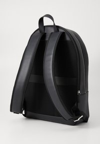 Zaino in pelle nera con finitura liscia, pannello posteriore in rete e spallacci imbottiti. Presenta una maniglia superiore e dettagli in zip argentata.