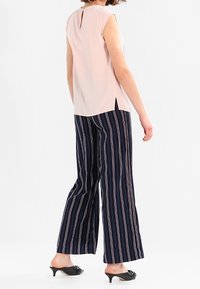 Light pink sleeveless top with a back keyhole and scalloped edges, paired with navy striped wide-leg pants and black slip-on shoes.