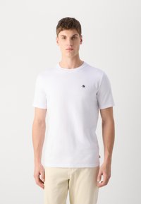 Hvid bomulds T-shirt med korte ærmer, rund halsudskæring og lille sort broderet logo på venstre bryst. Glat tekstur.