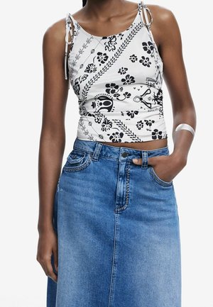 Débardeur à imprimé floral noir et blanc avec des bretelles ajustables à nouer, associé à une jupe en denim bleue taille haute avec une silhouette droite.