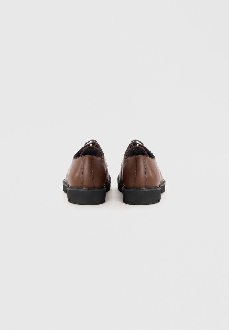 Zapatos de cuero marrón con un acabado suave, suelas de goma negra y diseño sin cordones, con bordes redondeados y acentos minimalistas.