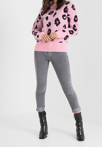 Maglione rosa con stampa leopardata nera e viola, abbinato a pantaloni in corduroy grigi e stivaletti neri lucidi. Tessuto morbido, design aderente.
