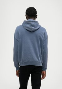 Sweatshirt com capuz em azul, feito de tecido macio, com um ajuste descontraído, ombros caídos e punhos e bainha canelados.
