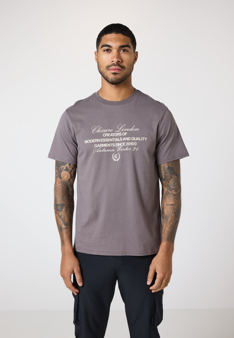 Graues Baumwoll-T-Shirt mit weißem Text, der Marken- und Kollektiondetails angibt, mit kurzen Ärmeln und lockerer Passform.