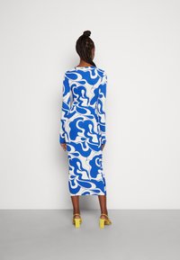 Robe moulante à manches longues avec un motif abstrait bleu et blanc. Elle présente un col rond et une jupe arrivant aux mollets.