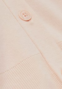 Cardigan rosa chiaro con una texture liscia, orlo a coste e un grande bottone rotondo vicino all'apertura.
