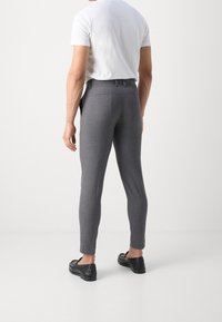 Šedé kalhoty na míru se slim fit střihem, vybavené pasem, poutky na opasek a bočními kapsami, v kombinaci s černými mokasíny a bílou košilí.