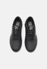 Sorte skinnesneakers med perforerte tåhetter, flate skolisser og en kontrasterende design på siden. Foret innside med logo på sålene.