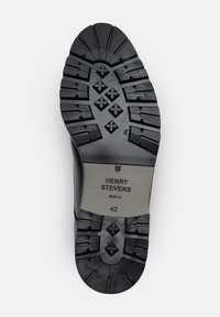 Semelle de chaussure en caoutchouc noir avec des crampons profonds, comportant une étiquette grise avec "HENRY STEVENS BERLIN" et la taille "42" en relief.