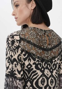 Schwarz-weiße Bluse mit Spitzenakzenten auf dem Rücken, aufwendigen floralem Mustern und einem Schlüsselloch-Ausschnitt am Hals.