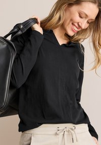 Zwarte langslavige top met een V-halsontwerp, gemaakt van zacht materiaal. Draag met crèmekleurige broek met trekkoord en metalen accenten.