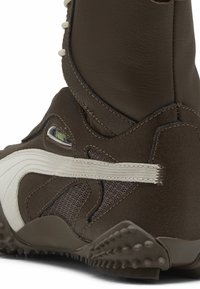 Zapato alto de cuero marrón y malla con un acento blanco, superficie texturizada y suela de goma con patrones de agarre prominentes.