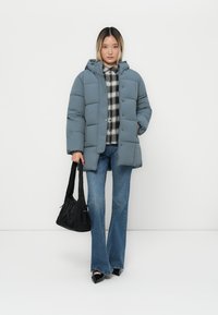 Gaiši zilas pūkaina jakas ar kapuci, slēgta ar pogām, uzvilkta virs melnbaltas pārsvītrotas krekliņa, saskaņota ar platām džinsiem un melnu somiņu.