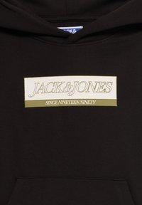 Sweat à capuche noir avec un patch rectangulaire affichant « JACK & JONES » et « SINCE NINETEEN NINETY » en texte contouré et plein.
