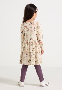 Floral print dress with long sleeves, ruffled hem, in beige, paired with purple ribbed leggings and white canvas shoes.