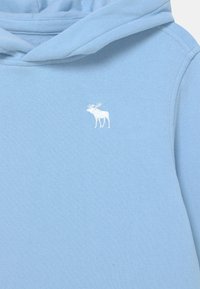 Jasnoniebieska bluza z kapturem wykonana z miękkiego materiału, z białym haftowanym logo łosia po lewej stronie klatki piersiowej. Kapelusz z zaokrąglonym dekoldem.