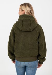 Oliwkowa polarowa bluza z kapturem o fakturowej powierzchni, z kapturem i ściągaczami. Krój jest krótki, z luźnym fasonem.