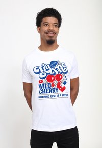 Vit bomulls-t-shirt med en färgglad grafisk design med röda körsbär, blå text och svarta prickar, med texten "Prova mig Vild Körsbär."