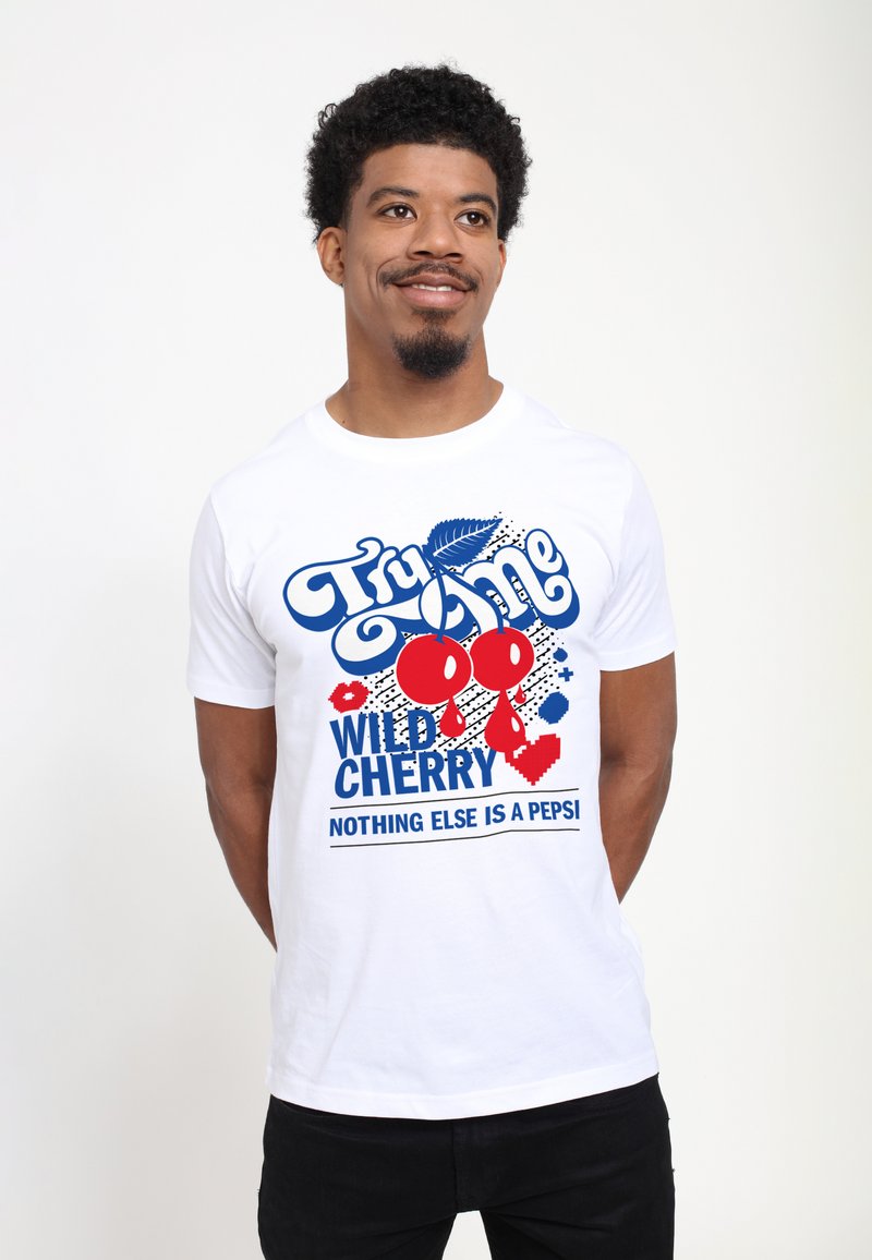 Vit bomulls-t-shirt med en färgglad grafisk design med röda körsbär, blå text och svarta prickar, med texten "Prova mig Vild Körsbär."