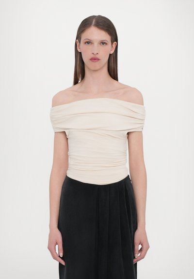 Top crème décolleté avec un design en tissu froncé, texture lisse et coupe ajustée, associé à une jupe noire fluide.