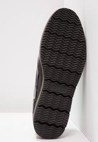 Sole di sneaker nera con un motivo a zigzag, materiale di gomma testurizzato e profilo laterale liscio.