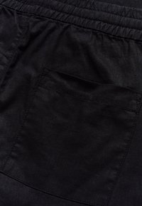 Prim-plan cu țesătură neagră, caracterizată printr-o talie elastică și un buzunar posterior cusut pe o pereche de pantaloni sau pantaloni scurți.