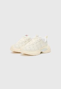 Des baskets crème avec un revêtement texturé, des perforations et des accents gris clair contrastants. Semelle en caoutchouc épaisse et design à lacets.