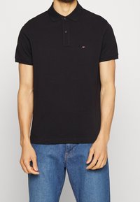 Schwarz polohemd mit Knopfleiste und kurzen Ärmeln. Hat ein kleines gesticktes Logo auf der linken Brust. Aus Baumwollmaterial.