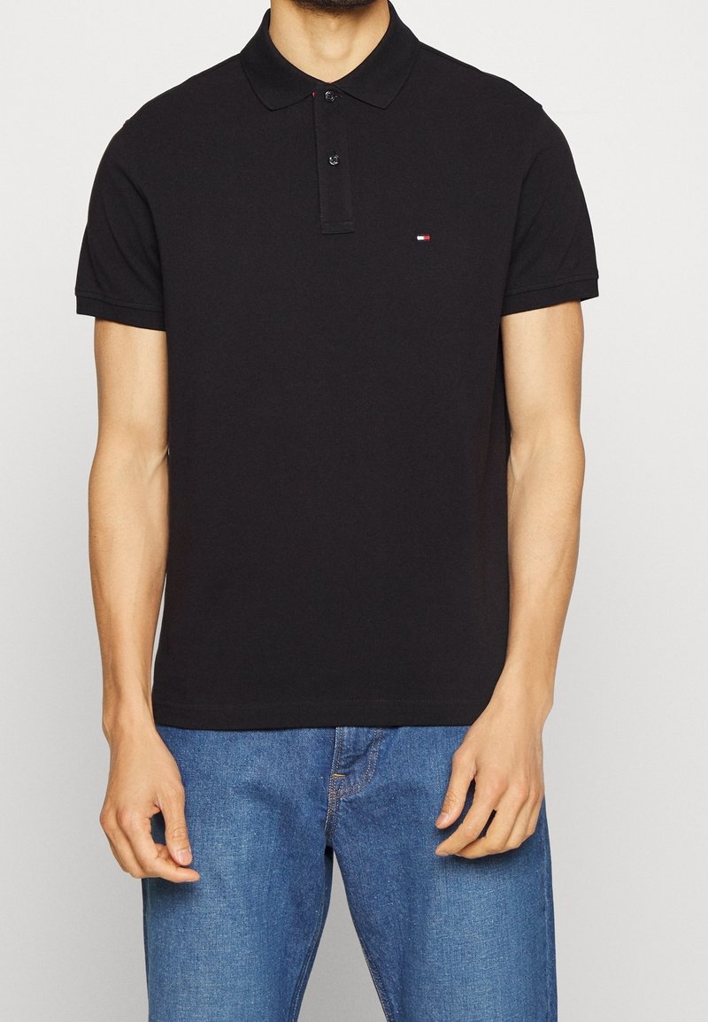 Schwarz polohemd mit Knopfleiste und kurzen Ärmeln. Hat ein kleines gesticktes Logo auf der linken Brust. Aus Baumwollmaterial.