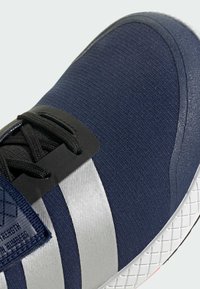 Námořnické modré sportovní boty s texturovanou tkaninou, černými tkaničkami a stříbrnými pruhy. Disponují elegantním designem a bílou vzorovanou podrážkou.