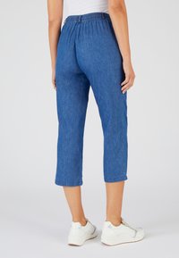 Pantalones de mezclilla azul cortos con cintura elástica, con un corte recto y dobladillos enrollados, combinados con zapatillas blancas.