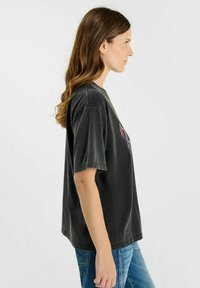 Camiseta de algodón negra de gran tamaño con mangas cortas, que presenta un colorido estampado gráfico en la parte delantera. Textura suave, corte relajado.