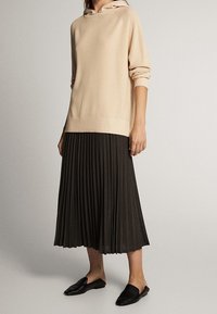 Sweat à capuche côtelé beige avec un cordon de serrage, associé à une jupe midi plissée foncée. Des ballerines noires complètent la tenue. Design simple et décontracté.