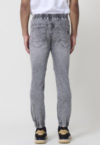 Joggers de denim gris con cintura elástica, tobillos ajustados y dos bolsillos traseros. Textura suave con un acabado desgastado. Combinados con zapatillas negras.