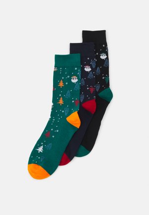 Drei Paar Socken: grün mit festlichen Mustern, schwarz mit Baum-Motiven und in einer einfarbigen dunklen Farbe, die an den Zehen farbige Akzente aufweist.