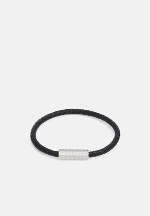Czarny pleciony skórzany bransoletka z fakturowaną srebrną zapięciem z grawerowanym logo. O okrągłym kształcie o gładkim wykończeniu.