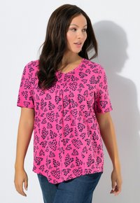 Top rosa a maniche corte con stampa a foglie nere, caratterizzato da scollo rotondo e pieghe per un dettaglio in più. Abbinalo a jeans di denim blu.