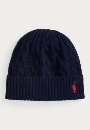 Navy knitted beanie with cable pattern and ribbed cuff. Features a small red logo on the front. Soft wool blend texture.