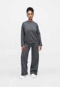 Sweatshirt cinza carvão e calças de perna larga feitas de material macio; apresentam punhos canelados e decote redondo. Combinados com ténis brancos.