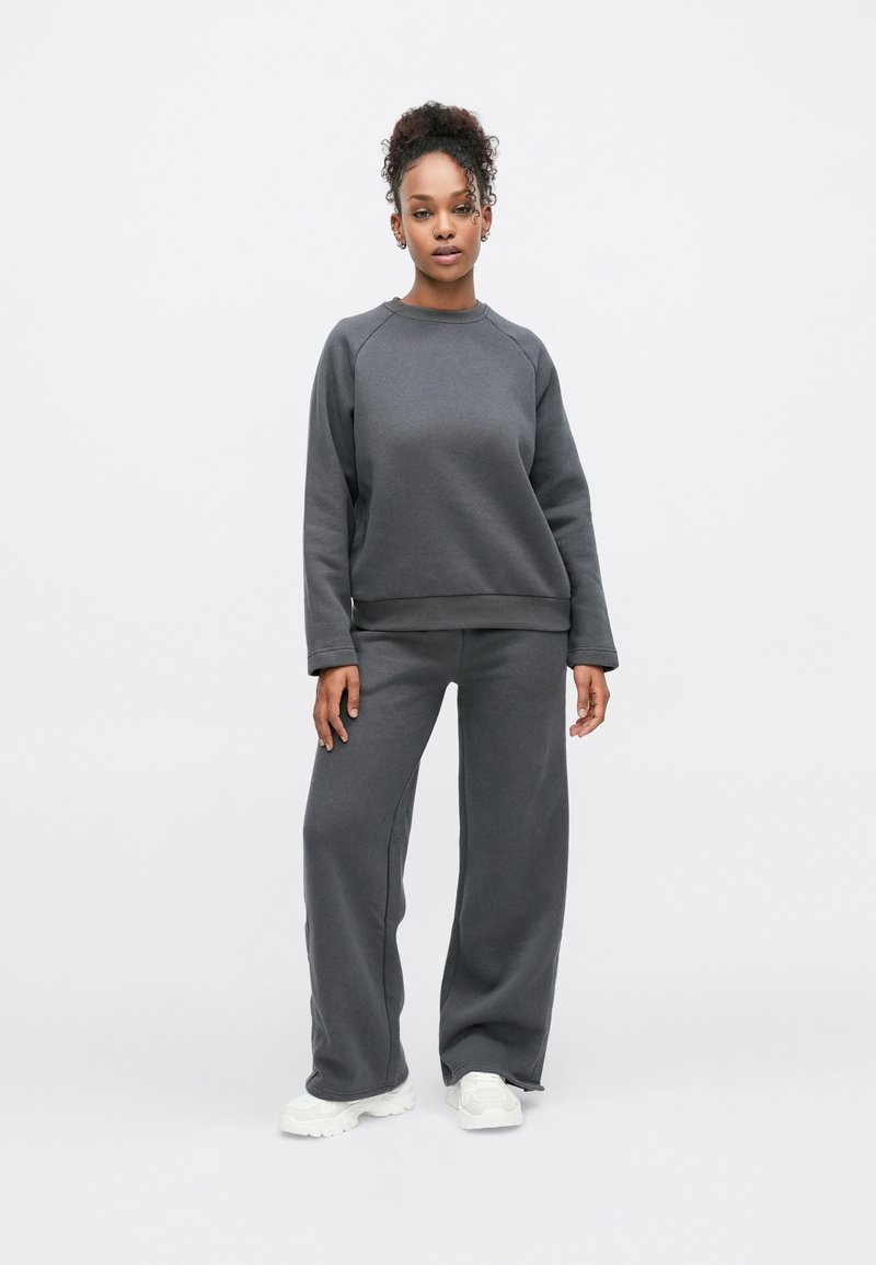 Sweatshirt cinza carvão e calças de perna larga feitas de material macio; apresentam punhos canelados e decote redondo. Combinados com ténis brancos.