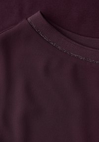 Sudadera burdeos con cuello acanalado y un detalle texturizado con un sutil brillo. Tejido suave y diseño ajustado que crean una silueta lisa.