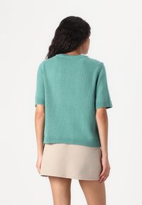 Light teal short-sleeve sweater with a ribbed hem. Soft knit texture. Worn over a beige skirt, showing a relaxed boxy fit.