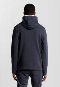 Donkergrijze hoodie van zacht materiaal, met een grote capuchon, lange mouwen en een losse pasvorm, met een gladde textuur en minimale details.